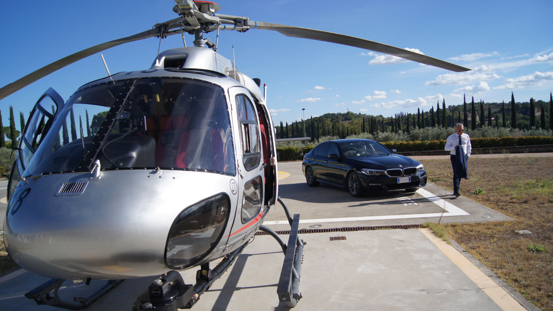 Massimiliano Dionisi, owner of The Roman Limousine Service, next to his luxury car and a helicopter