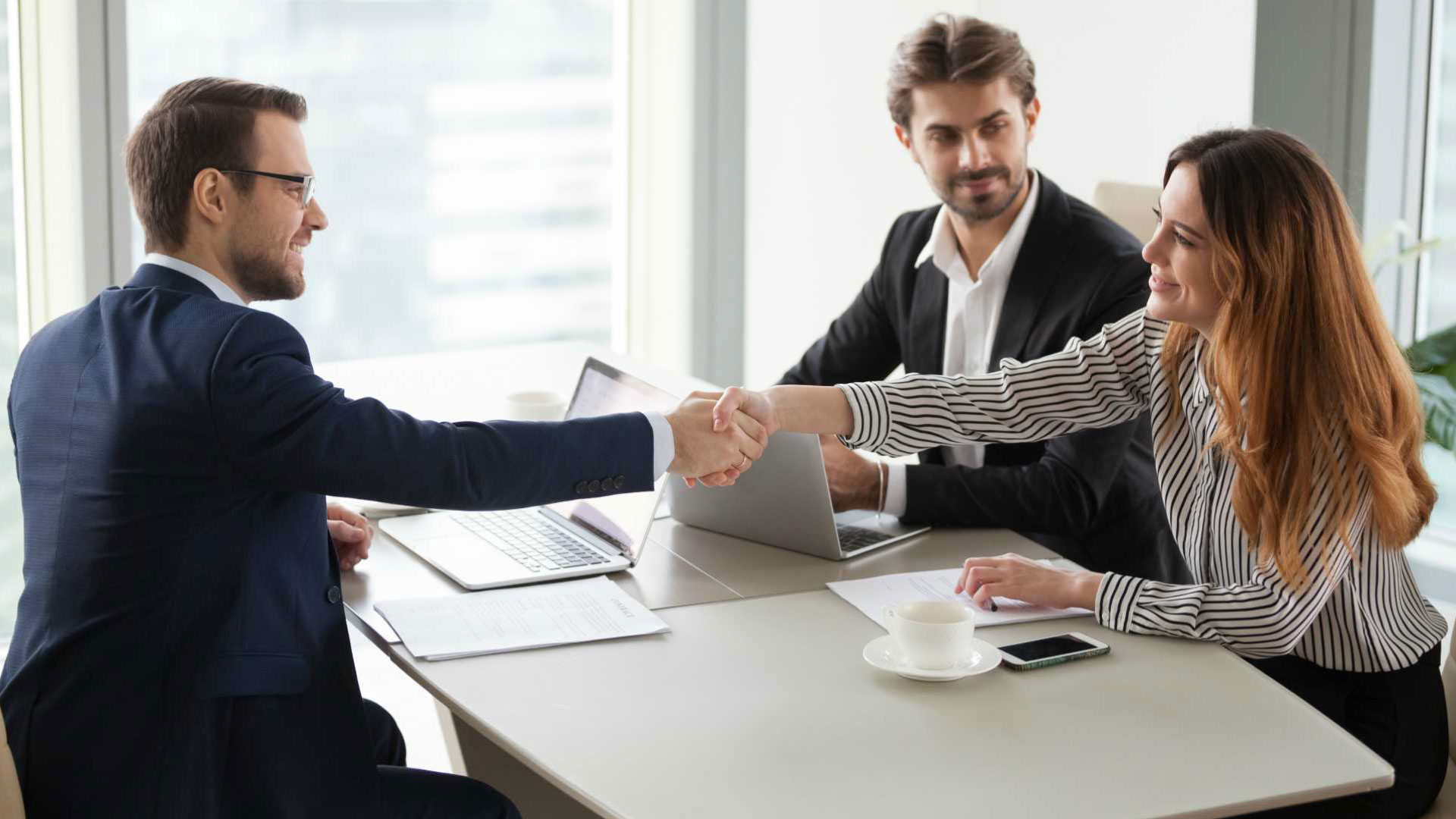 A salesperson and two buyers shaking hands in agreement, symbolizing successful deal closure and boosting your sales skills through effective communication and professionalism.