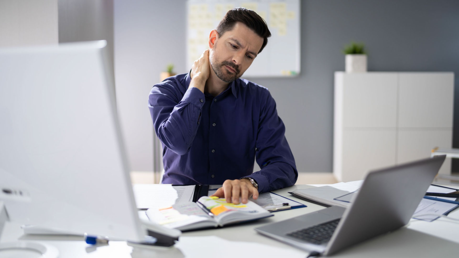 Office Chair Footrests: A man in an office experiencing neck pain, highlighting the importance of ergonomic footrests for improving posture and reducing discomfort.