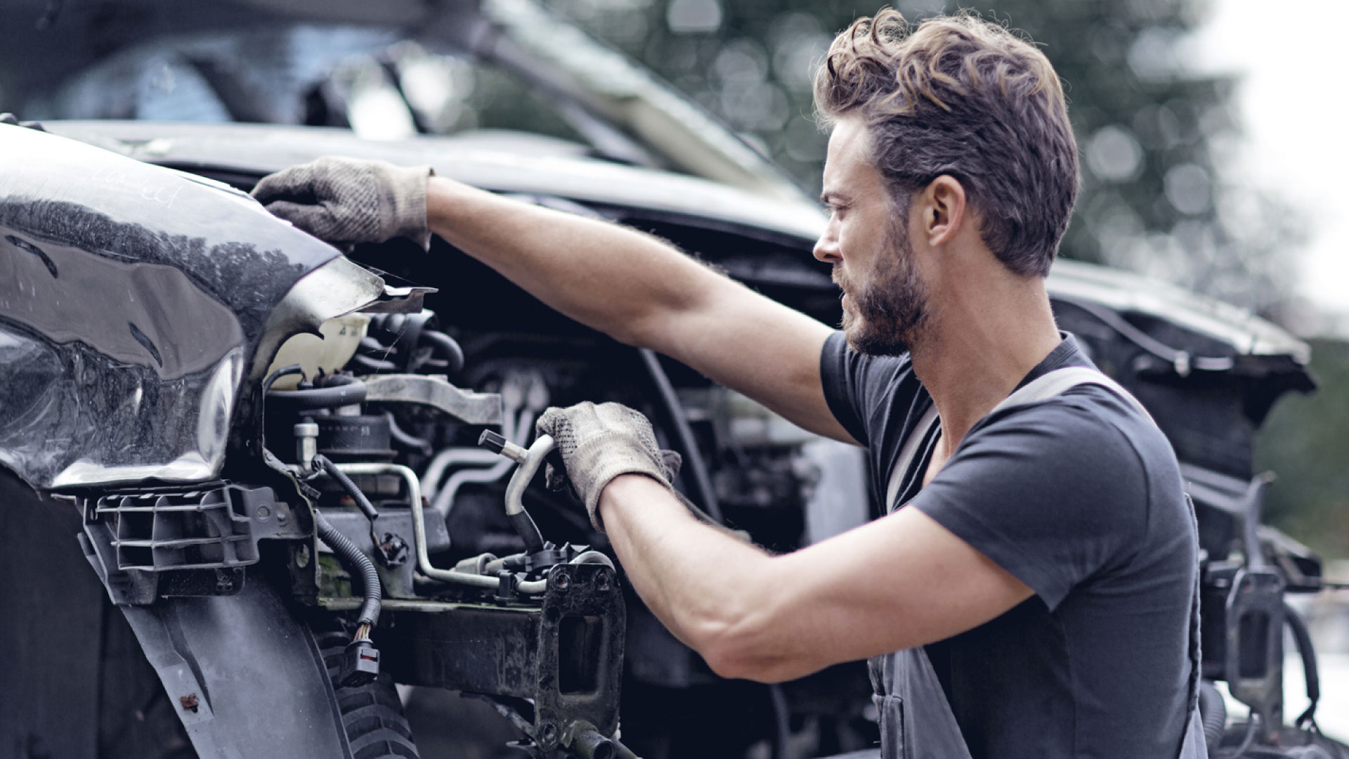 A man removing engine parts from a car, representing the vital role of car wreckers in recycling auto parts and promoting sustainability.